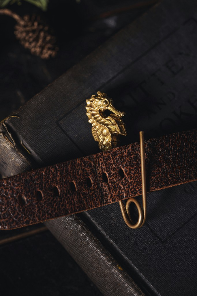 Gold seahorse clasp on brown leather strap over a worn book